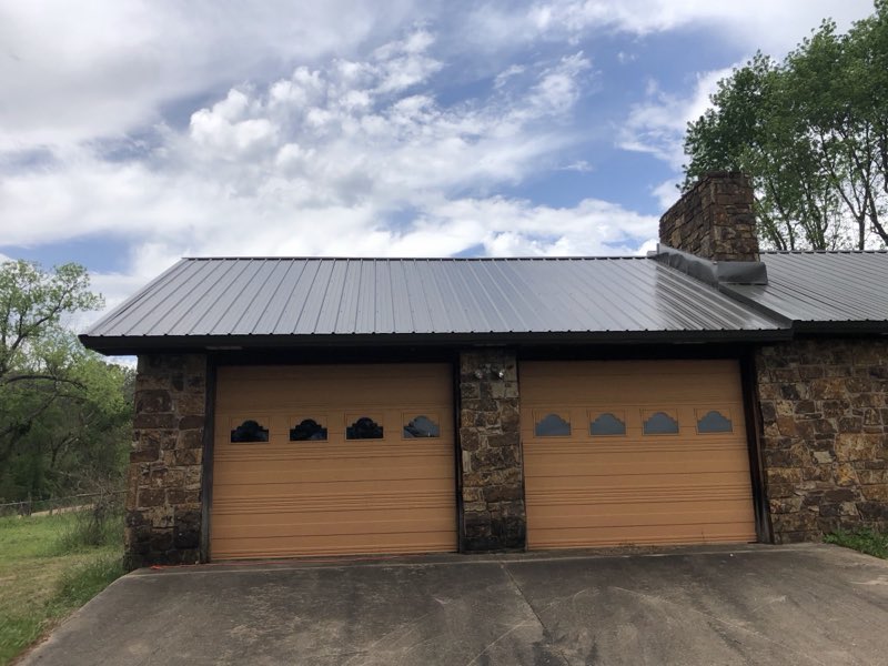Stone garage with new overhead doors and a gray metal roof